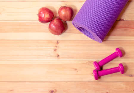 Purple yoga mat, pink dumbbells and red apples on wooden background. Top view with copy space.の写真素材