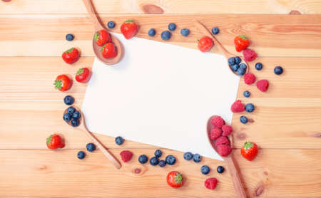 Empty card for your text surrounded by fresh berries and berries in wooden spoons on woodenの写真素材