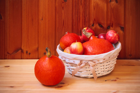 Orange pumpkins and red apples in white wicker basket on wooden table. Selective focus. View with copy space.の写真素材