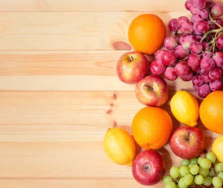 Fresh ripe apples, lemons, oranges and grape as border on wooden background. Top view, copy space.の写真素材