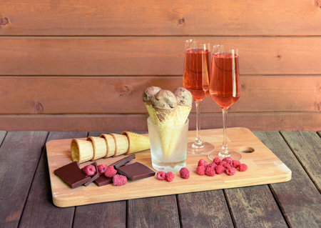 Glasses of rose champagne, waffle cones with chocolate ice cream in glass as stand, pieces of dark...