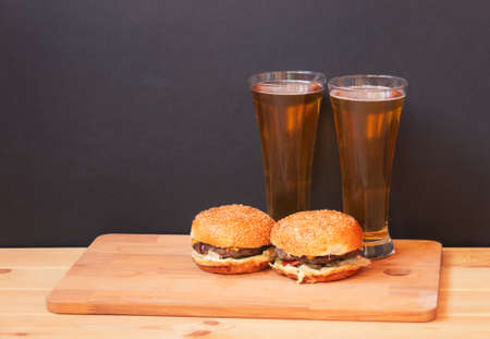 Glasses of beer and burgers on wooden table on dark background. View with copy space.の写真素材