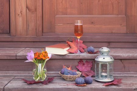 Glass of rose champagne, book, lantern, figs, helenium and and autumn crocuses on steps of rustic...