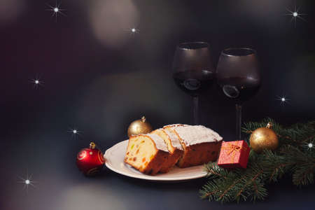Christmas cake with candied fruits and raison, two glasses of red wine, fir branches and christmas decorations on dark background. View with copy space.の写真素材