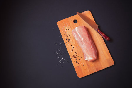Raw pork meat. Fresh fillet on cutting board on dark background. Top view, copy space.の写真素材
