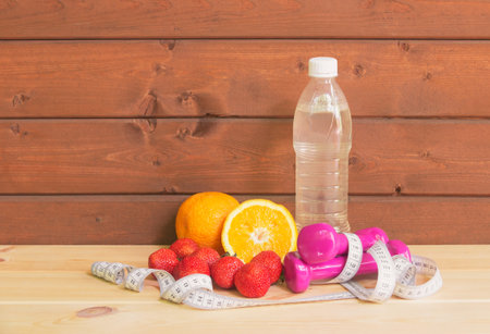 Dumbbells, bottle of water, fresh oranges, strawberry and measure tape. Fitness and healthy eating...