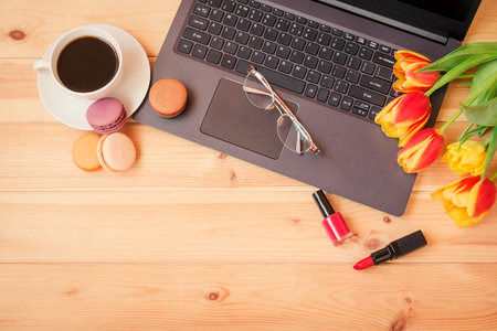 Laptop keyboard, coffee cup, glasses, lipstick, nail polish and  tulip flowers on wooden table.の写真素材