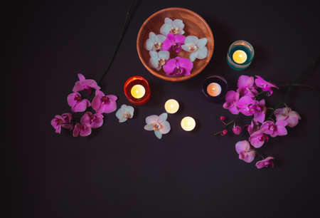 Colorful orchids and burning candles on dark background. Top view, copy space.の写真素材