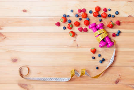Two pink dumbbells, measuring tape and berries on wooden background. Top view, copy space.の写真素材