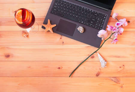Laptop, glass of sangria, branch of orchid, starfish and seashells on wooden table. Summer holidays or freelance concept. Top view, copy space.の写真素材
