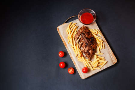 Baked pork ribs with french fries on cutting board on dark background. Top view, copy space.の写真素材