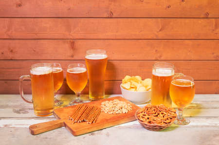 Mugs of beer, glasses of beer and beer snacks on cutting board on aged wooden table. View with copy space.の写真素材