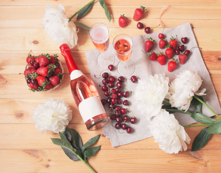 Bottle of rose champagne, glasses of rose champagne, white peonies, fresh cherry and  strawberry on wooden table. Top view.の写真素材
