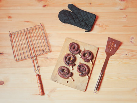 Roasted sausages, grid, spatula and glove for barbecue and grill on wooden background. Top view.