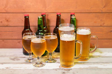 Mugs, glasses and bottles with beer on aged wooden table.の写真素材