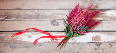 Bouquet of beautiful red and pink astilbe flowers with red ribbon on aged wooden background. View...