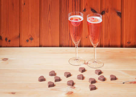 Two glasses of rose champagne and heart shape chocolate candies on wooden table. Selective focus. View with copy space.の写真素材