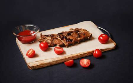 Baked pork ribs and tomato ketchup on cutting board on dark background. Selective focus.の写真素材