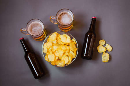 Mugs of beer, bottles of beer and bowl with potato chips on gray background. Top view.の写真素材