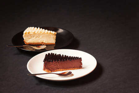 Classical cheesecake with creamy sauce and chocolate cheesecake with chocolate sauce on dark background. Selective focus on chocolate cheesecake. View with copy space.の写真素材