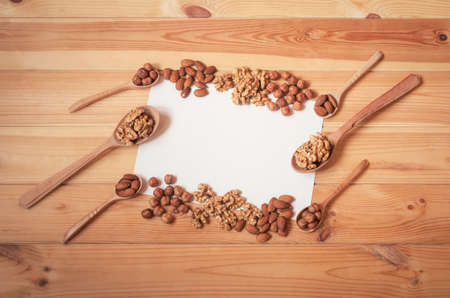 Hazelnuts, walnuts and almonds in wooden spoons and near around empty card for your text on wooden table. Top view, copy space.の写真素材