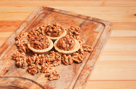 Cakes with walnuts and caramel and walnuts near on cutting board on wooden table. Selective focus.