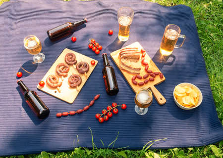 Picnic with beer glasses and mugs, beer bottles, roasted sausages, potato chips, bread and little chorizo sausages. Top view.の写真素材