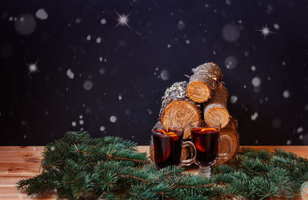 Glasses of mulled wine, fir branches and pile of firewood on dark background. View with copy space.の写真素材