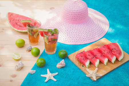 Watermelon mojito cocktail on wooden table in sunny day. Watermelon, limes, starfishes, seashells and hat near. Selective focus.の写真素材