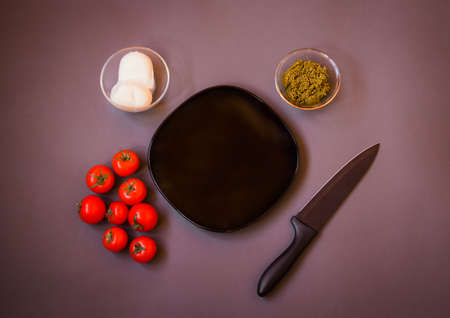 Tomatoes, pesto sauce and mozzarella cheese for making caprese salad around empty plate on gray background. Top view, copy space.の写真素材