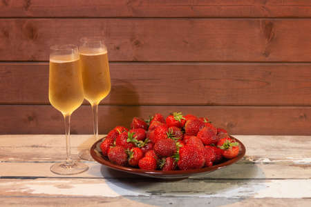 Two glasses of champagne and fresh strawberry on brown plate on aged wooden table. Selective focus.の写真素材