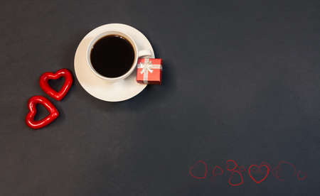 Cup of coffee, gift box and two red hearts on dark background. Top view, copy space.の写真素材