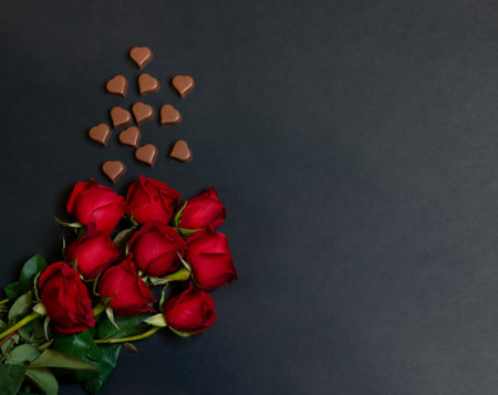 Valentine's day concept. Border of heart shape chocolate candies and red roses on dark background. Top view, copy space.の写真素材