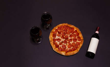 Delicious pepperoni pizza, bottle of red wine and glasses of red wine on dark background. Top view, copy space.の写真素材