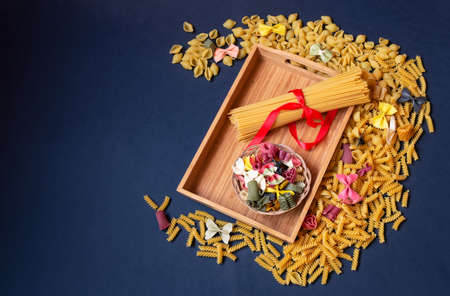 Wooden tray with raw pasta surrounded by different kinds of raw pasta on dark background. Top view with copy space.の写真素材