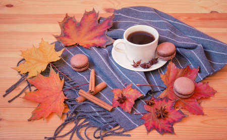 White cup of coffee, gray scarf, chocolate macaroons, spices and autumn leaves on wood. selective focus.の写真素材