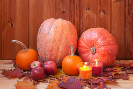 Orange pumpkins, red apples, candles and colorful maple leaves on wooden table.の写真素材