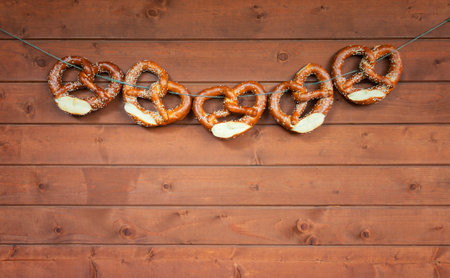 Freshly baked pretzels hanging on clothesline against wooden board.の写真素材
