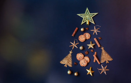 Christmas tree made from golden winter decorations, cookies and spices on dark background with empty...