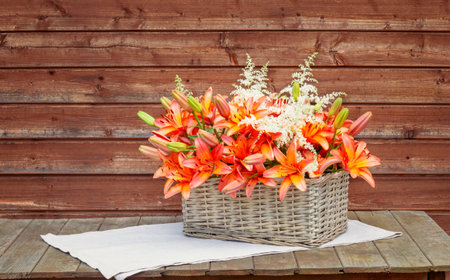 Wicker basket with orange lilies and white astilbe flowers on wooden table. view with copy space.の写真素材