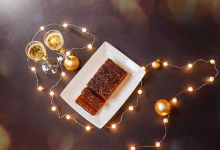 Glasses of champagne, chocolate cake, christmas balls and glowing christmas lights on dark background. top view.の写真素材