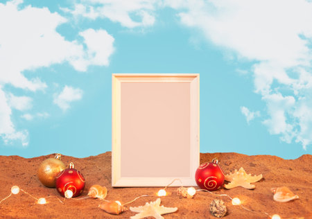 White frame, chrismas balls, glowing christmas lights, starfishes and seashells on sand beach. Christmas and New Year celebration. view with copy space.の写真素材
