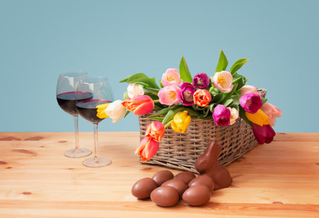 Easter concept. Colorful tulips, chocolate bunny, glasses of red wine and chocolate Easter eggs on wooden table.の写真素材