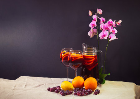 Red wine sangria with fruits in glasses and pitcher on table. Fresh fruits and purple orchid near. dark background. view with copy space.の写真素材