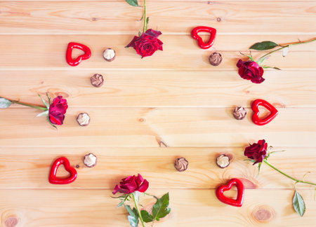 Frame made from red roses, red hearts and chocolate candies on wooden background. Top view, copy space.の写真素材