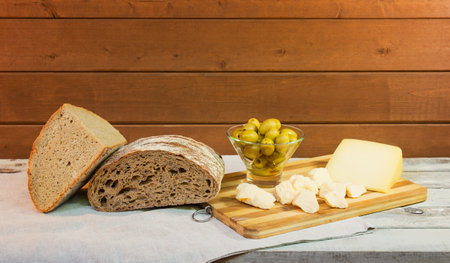Rye bread, green olives and cheese on cutting board on aged wooden table. view with copy space.の写真素材