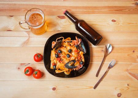 Pappardelle pasta with seafood with tomato sauce, mug of beer and bottle of beer on wooden table. top view.の写真素材