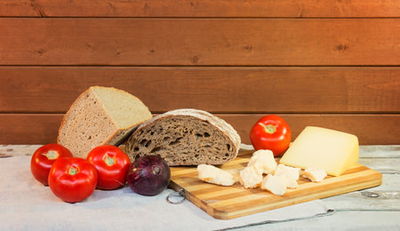 Rye bread, vegetables and cheese on cutting board on aged wooden table. view with copy space.の写真素材