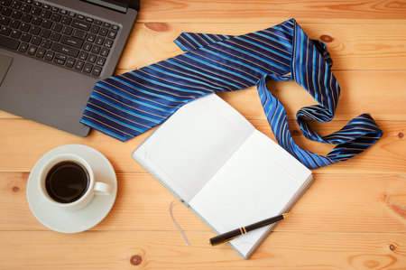 Opened diary, necktie, cup of coffee, laptop and pen on wooden table. Top view, copy space.の写真素材