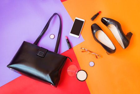 Black leather bag, black shoes, smartphone, glasses and cosmetics on colorful background. Top view, copy space.の写真素材